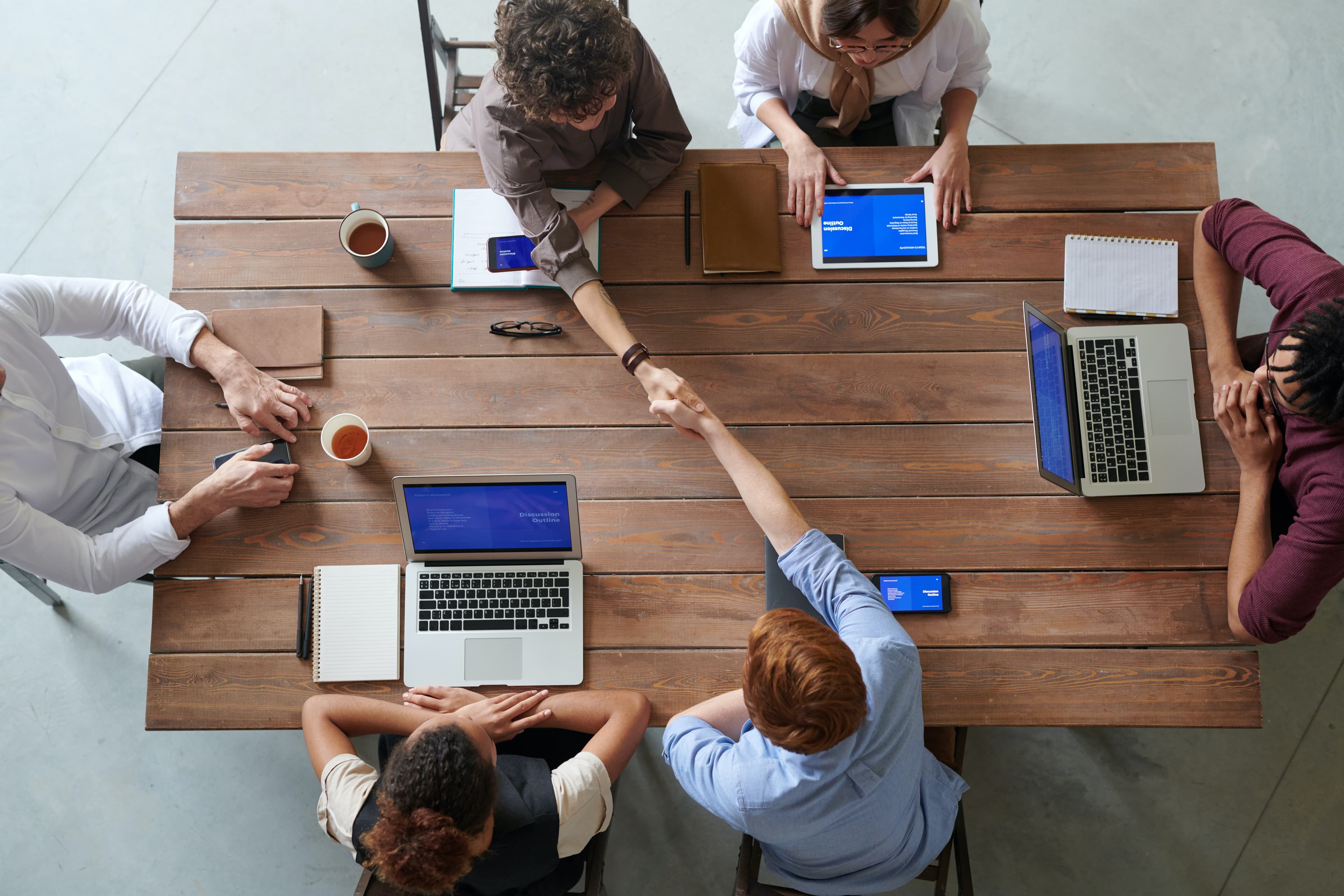 A group of people with laptops sitting around a wooden table. Photo by fauxels from Pexels.